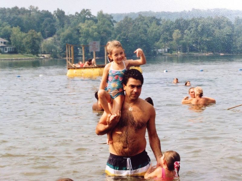 Young Danielle riding on her father's shoulders in a lake